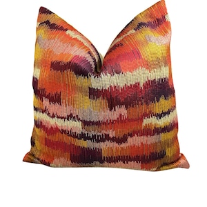 May include: A decorative throw pillow with a vibrant, abstract pattern. The pillow features a woven design in shades of orange, red, yellow, and purple. The pillow is square-shaped and has a textured appearance, adding visual interest to any room.