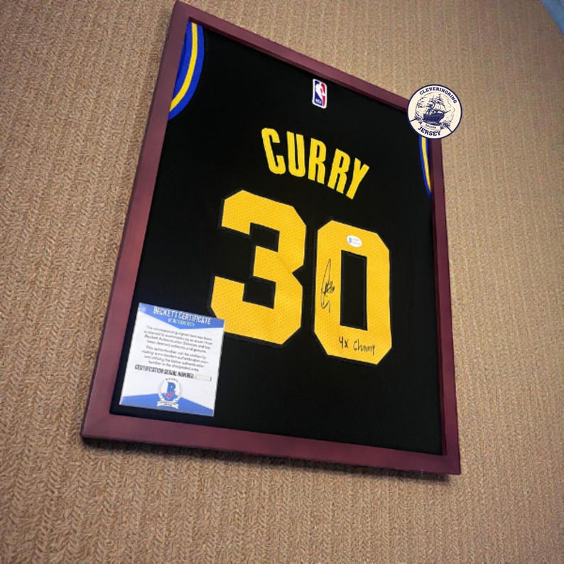 K&ouml;nnte beinhalten: Gerahmtes schwarzes Basketballtrikot mit dem Namen "CURRY" und der Nummer "30" in Gelb. Das Trikot ist signiert und enth&auml;lt "4x Champ". Der Rahmen ist dunkelburgunderfarben.