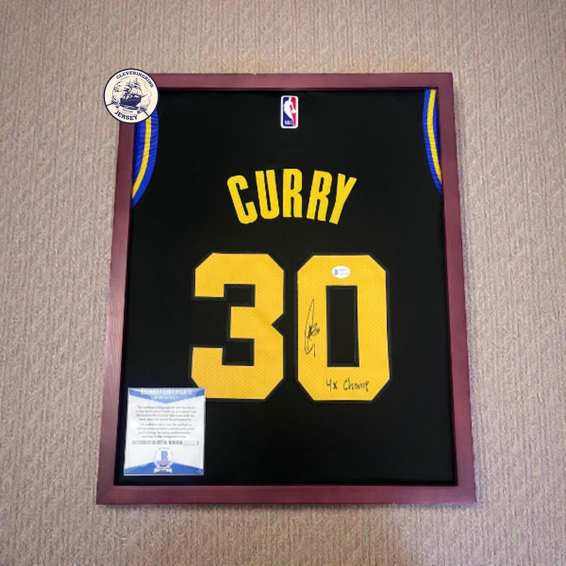 K&ouml;nnte beinhalten: Gerahmtes schwarzes Basketballtrikot mit goldenen Buchstaben und Zahlen. Das Trikot tr&auml;gt den Namen "CURRY" und die Nummer "30". Enth&auml;lt eine Unterschrift und den Text "4x Champ". Der Rahmen ist braun mit einem weinroten Innenraum.