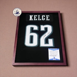 May include: Framed black jersey with the name "KELCE" and the number "62" in white. The jersey is signed and includes a Beckett Certificate of Authenticity. The frame is a dark burgundy color.