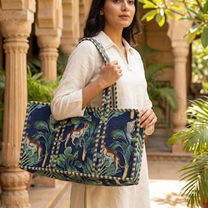 May include: A rectangular tote bag featuring a dark blue background with a repeating pattern of leopards and green tropical palm leaves. The bag has two matching fabric shoulder straps and a structured, quilted design with green and white striped trim.