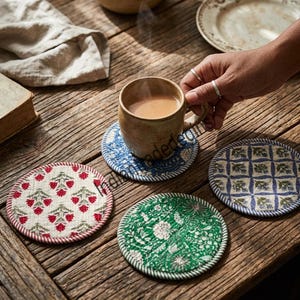 May include: Four round fabric coasters featuring quilted textures and distinct patterns. One coaster is white with red floral motifs, one is green with white floral prints, one is blue with white patterns, and one is white with a blue grid and floral design.