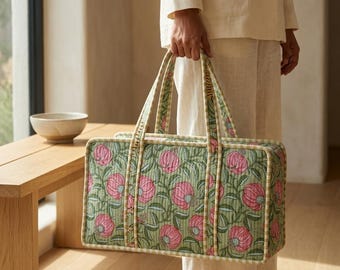May include: A rectangular quilted tote bag featuring a sage green background with a repeating pattern of pink pomegranate-like fruits and dark green leaves. The bag has two matching fabric handles and light-colored striped piping along the edges.