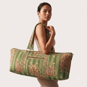 May include: A rectangular quilted duffel bag in a sage green hue, featuring a repeating pattern of orange and black tigers. The bag includes two long shoulder straps, a horizontal zippered pocket on the front, and a top zipper closure.