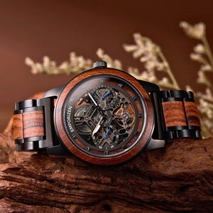 Puede incluir: Un reloj de pulsera de madera con caja negra y esfera esqueleto. El reloj presenta un bisel y una correa de madera marrón, mostrando los intrincados mecanismos internos. El reloj se exhibe sobre un trozo de madera.