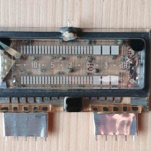 Peut inclure: Composant électronique vintage avec un écran rectangulaire. L'écran affiche des barres verticales et des marquages numériques, dont "10, 5, 2, 0, 3 dB". Le composant a des connecteurs métalliques et est posé sur une surface en bois.