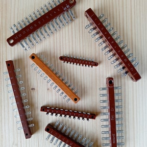 Op de afbeelding: Een assortiment vintage elektrische klemmenstroken. De stroken zijn voornamelijk bruin met zilverkleurige metalen contacten. Sommige stroken hebben nummers en zijn gerangschikt op een lichtgekleurd houten oppervlak.