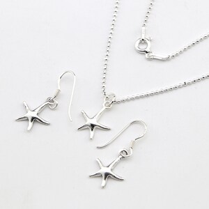 Puede incluir: Un conjunto de joyas de plata con forma de estrella de mar, que incluye un collar y dos pares de pendientes. El collar presenta una delicada cadena de bolas y un colgante de estrella de mar. Los pendientes tienen un diseño de gancho.