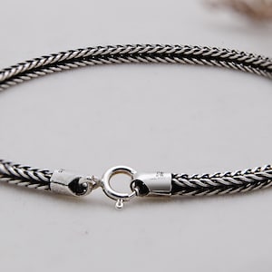 May include: A silver-colored bracelet with a woven design. The bracelet has a secure clasp and is approximately 7 inches in circumference. The jewelry is made of a shiny, metallic material and is suitable for everyday wear.