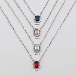 Peut inclure: Quatre colliers en argent avec des pierres précieuses carrées de différentes couleurs. Les pierres précieuses sont bleues, roses, blanches et rouges. Chaque collier a une petite bordure en forme de diamant autour de la pierre précieuse. Les colliers sont étiquetés "Style 1", "Style 2", "Style 3" et "Style 4".