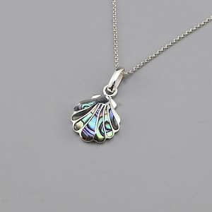 Può includere: Una collana d'argento con un ciondolo a forma di conchiglia. Il ciondolo ha un intarsio di madreperla con colori iridescenti blu, verdi e viola. La catena è delicata e il ciondolo misura circa 2,5 cm di larghezza.