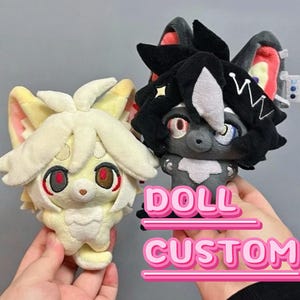 May include: Two plush dolls with anime-style features. One is cream-colored with red eyes, the other is gray with black hair and red and blue eyes. The dolls have large ears and are labeled "DOLL CUSTOM" in pink text.