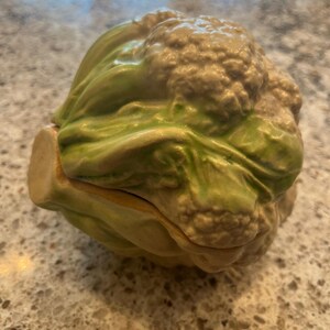 Pode incluir: Um prato de cerâmica em forma de couve-flor com um esmalte verde e branco. O prato está aberto e parece ser um prato para servir.