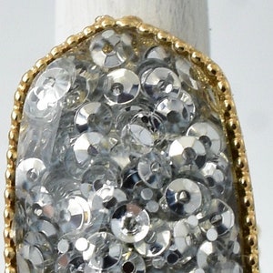 Puede incluir: Un anillo de oro con una piedra ovalada transparente llena de lentejuelas plateadas.