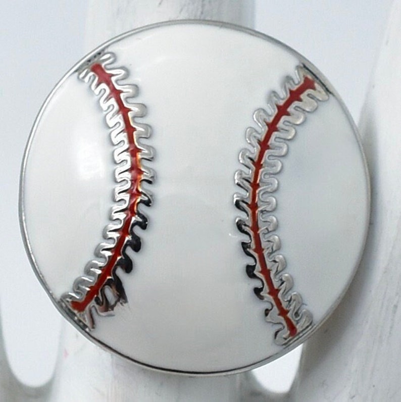 May include: A round baseball-themed charm with a white background and red stitching. The charm has a silver-colored border. This baseball charm is a great accessory for sports fans.