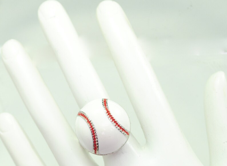 May include: A baseball-themed ring featuring a white ball with red stitching and a silver-colored band. The ring is a sporty accessory, perfect for baseball fans.