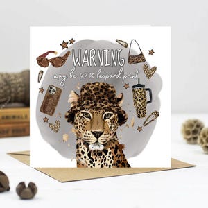 May include: Greeting card with a leopard wearing a leopard print hat. The card reads "WARNING may be 97% leopard print". Leopard print accessories, such as sunglasses, a phone case, and a handbag, surround the leopard.