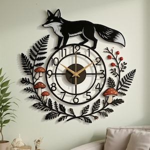 May include: A black wall clock featuring a fox silhouette on top, surrounded by a decorative frame of black fern leaves, red berries, and mushrooms. The clock face has black numbers and gold-coloured hands, creating a detailed nature-inspired design.