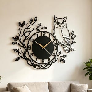 May include: A black wall clock featuring a circular face with gold hands and numbers one through twelve. The clock is integrated into a metal cutout design of a perched owl on a branch surrounded by intricate tree branches and leaves.
