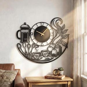 Puede incluir: Un reloj de pared de metal negro con esfera circular y manecillas doradas, rodeado de recortes decorativos de una prensa francesa, cucharas, tazas, bolsitas de té y ramas de cafeto con hojas y bayas dispuestas en un diseño semicircular.