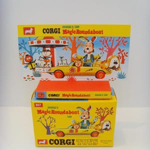 Puede incluir: Una caja amarilla con tapa roja y una imagen de un coche amarillo con un conejo y un perro en ella. La caja dice "Corgi Toys" y "Dougal's Magic Roundabout Car". La caja es para un coche de juguete.
