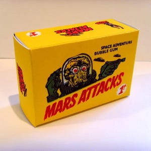 May include: A yellow box with a red and white graphic of a Martian holding a gun. The box says "Space Adventure Bubble Gum" and "Mars Attacks!" with a number "1" on the front.