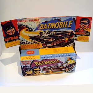 May include: A vintage die-cast toy Batmobile box with a rocket firing feature. The box is purple, blue, and yellow with images of Batman and Robin. The text on the box reads "Rocket Firing Batmobile Die-Cast Scale Models Playcraft Toys Ltd. - London".