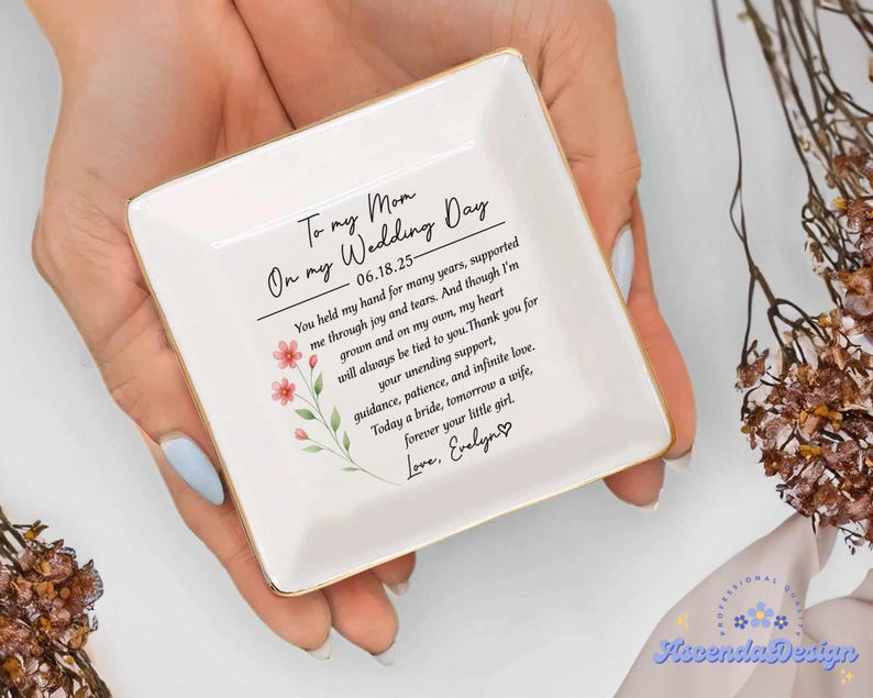 May include: A square, white ceramic trinket dish with gold trim, held in a person's hands. The dish features a floral design and a heartfelt message: "To my Mom On my Wedding Day." The text includes a date and a personal note.