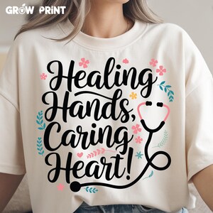 May include: White t-shirt with black text that reads "Healing Hands, Caring Heart!" with a pink stethoscope graphic and pink floral accents.