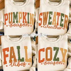 Może przedstawiać: Cztery kremowe bluzy z jesiennym tekstem w kolorze pomarańczowym, zielonym i żółtym. Bluzy mają napisy "Pumpkin Season", "Sweater Weather", "Fall Vibes" i "Cozy Season" w stylu retro.