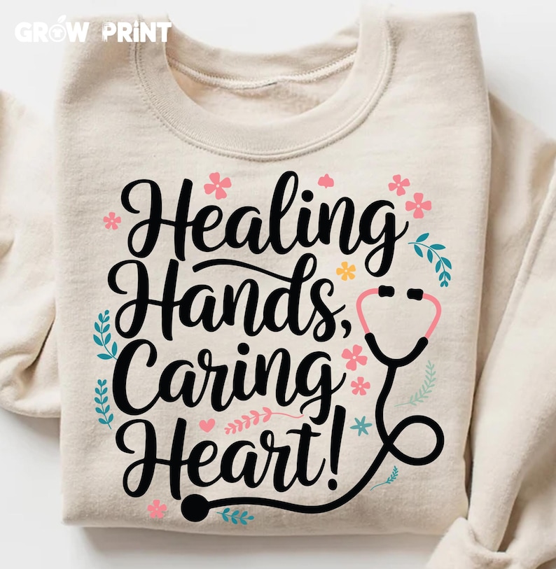 May include: A beige sweatshirt with the text "Healing Hands, Caring Heart!" in black lettering. The text is surrounded by pink and blue flowers and a black and pink stethoscope.
