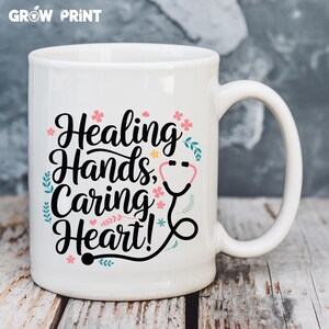 May include: White ceramic mug with a black design that says "Healing Hands, Caring Heart!" with a stethoscope graphic and pink and blue floral accents.