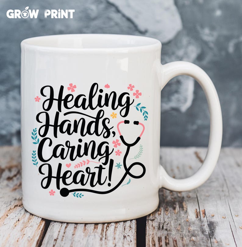 May include: White ceramic mug with a black design that says "Healing Hands, Caring Heart!" with a stethoscope graphic and pink and blue floral accents.