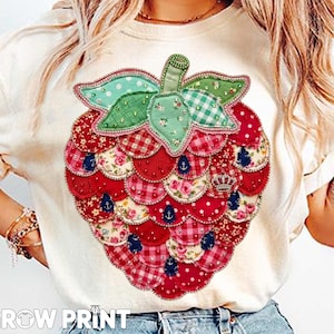Puede incluir: Camiseta color crema con un gran diseño de fresa colorida. La fresa está hecha de varios patrones de tela, incluyendo lunares, estampados florales y cuadros. El diseño incluye una pequeña corona y detalles de ancla. El texto "GROW PRINT" está en la parte inferior.