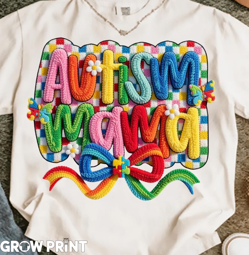 May include: White t-shirt featuring the words "Autism Mama" in colorful, textured letters. The design includes a rainbow bow, flowers, and butterflies, all set against a checkered background. The brand name "GROW PRINT" is printed at the bottom.