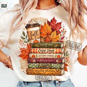 Puede incluir: Una camiseta de color crema con un gr&aacute;fico de una pila de cinco libros coronada por una taza de caf&eacute;. Los libros est&aacute;n etiquetados como Crisp Air, Cozy Days, Autumn Stories, Pumpkin Spice y Sweater Weather, rodeados de hojas de oto&ntilde;o y bayas.