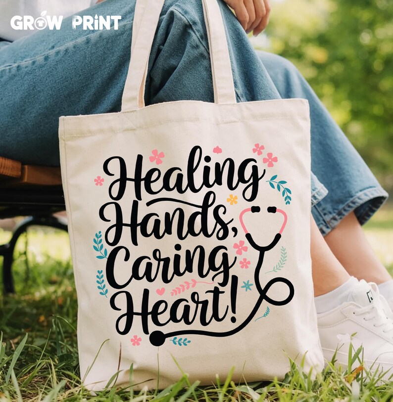 May include: A white canvas tote bag with black text that reads "Healing Hands, Caring Heart!" and a black stethoscope graphic. The bag has pink and blue floral accents.