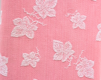 Puede incluir: Tela rosa con un patrón floral blanco. La tela tiene una superficie texturizada y las flores están en relieve.
