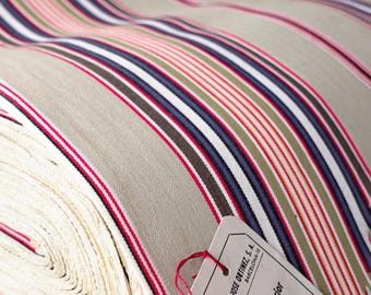 Peut inclure: Un rouleau de tissu à rayures beiges, roses, rouges, vertes, bleues et marron. Le tissu présente un aspect texturé et une étiquette attachée avec du texte. Les rayures sont disposées en diagonale sur le tissu.
