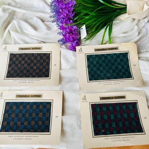 May include: Four vintage fabric swatch cards with the text "FRANELA ALPINA" and "PURO ALGODON GARANTIZADO COLORIDO SOLIDO". The swatches feature woven patterns in various colors, including green, blue, and brown. A bouquet of purple flowers and green foliage are in the background.