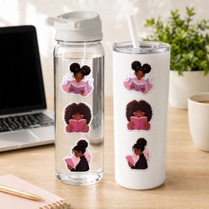a clear water bottle and a white tumbler with stickers on them, placed on a wooden desk next to a laptop and a plant.