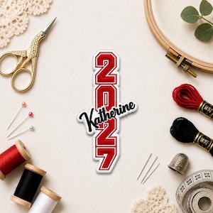 May include: A red and white patch with the text "2027 Katherine" in a collegiate style. The patch is surrounded by sewing supplies, including scissors, thread, needles, and a measuring tape.
