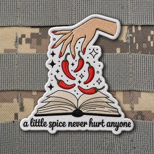 May include: Embroidered patch featuring a hand with red fingernails sprinkling red chili peppers over an open book. The text "a little spice never hurt anyone" is at the bottom. The patch has a white border and is set against a camouflage background.