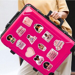 A person is holding a pink suitcase with various stickers on it.