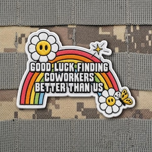 May include: Embroidered patch with the text "GOOD LUCK FINDING COWORKERS BETTER THAN US" over a rainbow. The patch features two smiling daisy flowers and a yellow butterfly. The patch is on a camouflage background.
