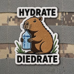 May include: Embroidered patch featuring a cartoon capybara holding a water bottle. The patch has the words "HYDRATE" and "DIEDRATE" in white block letters. The capybara is brown with a white outline, and the water bottle is blue.