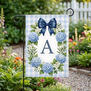 May include: A garden flag featuring a blue gingham background. The flag displays a wreath of blue hydrangeas and white flowers around a letter "A". A navy blue bow sits at the top.