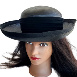 May include: A black hat with a wide brim and a rounded crown. The hat features a black velvet band around the crown. The brim is slightly curved, and the hat appears to be made of a woven material. The hat is displayed on a mannequin head.