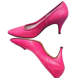 May include: Two bright pink leather pumps with pointed toes and small heels. The shoes have a classic design with a smooth texture. The heels are approximately 2 inches tall.