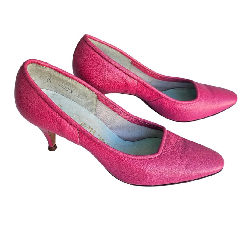 May include: A pair of bright pink leather pumps with a pointed toe and a low, kitten heel. The shoes have a textured surface and a light blue interior. The heels measure approximately 2 inches.